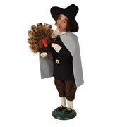 A decorative figurine of a historical pilgrim holding a feathered turkey, standing on a round base against a plain white background.