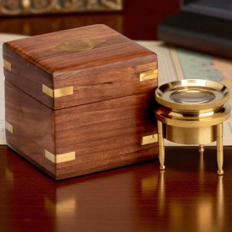 Wooden box with gold accents and a brass magnifying glass on a wooden surface.
